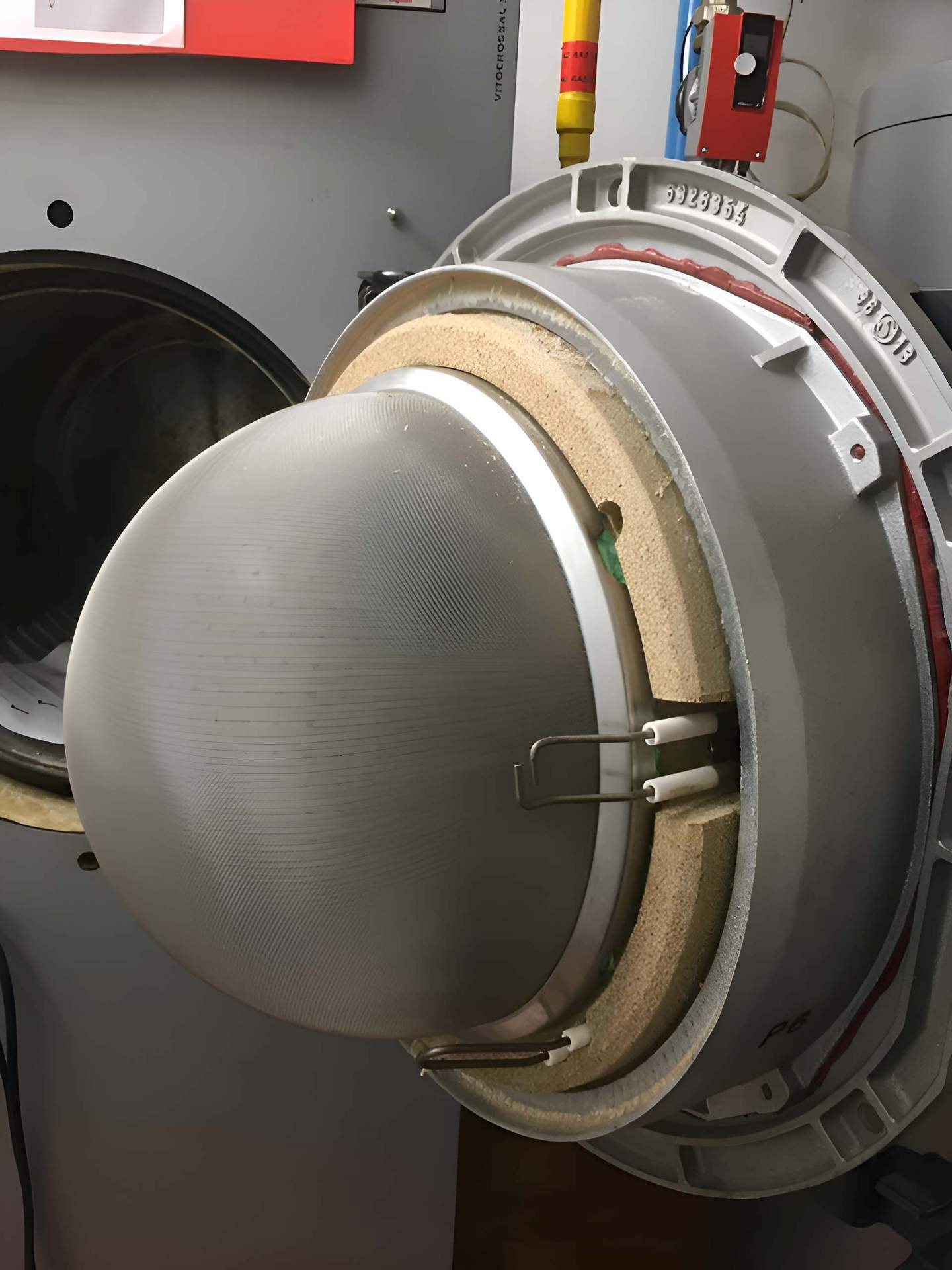 Gros plan sur un brûleur en métal gris démonté d’une machine industrielle, avec son isolant réfractaire et ses électrodes blanches.